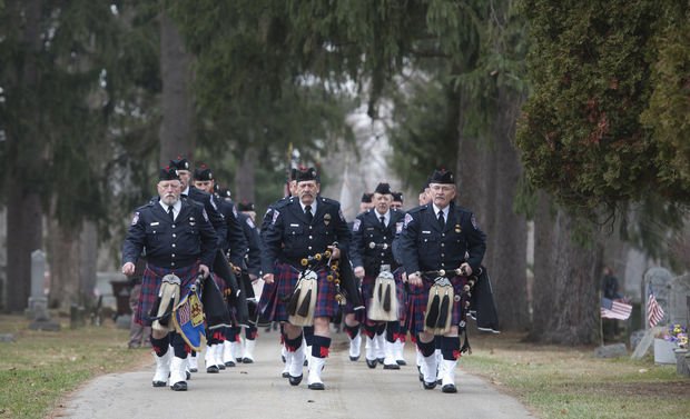 The band leads a funeral procession through a tree-lined cemetery